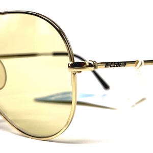 May include: Gold-tone aviator sunglasses with yellow lenses. The sunglasses feature a double bridge and the brand name "CEBE" printed on the temple. The lenses are a light yellow color, and the frames are a shiny gold.