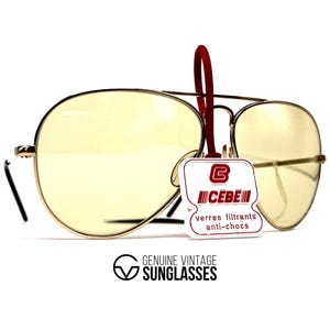 May include: Vintage aviator sunglasses with gold frames and yellow-tinted lenses. The glasses have a double bridge and black temples. A red tag with the brand name "CEBE" is attached. The text "GENUINE VINTAGE SUNGLASSES" is printed below.