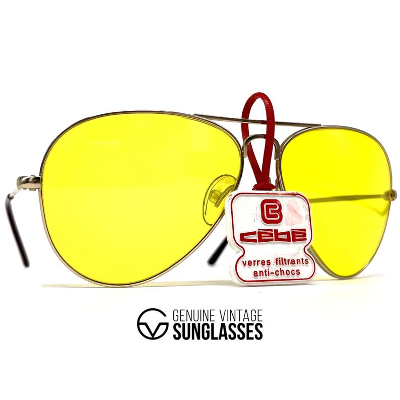 Puede incluir: Gafas de sol aviador vintage con lentes amarillas brillantes y montura plateada. Las gafas de sol tienen una etiqueta roja adjunta con la marca "CEBE" y el texto "verres filtrants anti-chocs". El texto "GENUINE VINTAGE SUNGLASSES" est&aacute; impreso debajo.