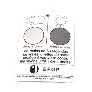 Puede incluir: Etiqueta rectangular blanca con una cuerda, con ilustraciones de una nube y un sol, y texto en franc&eacute;s. El texto describe gafas de sol que se oscurecen con la luz solar y protegen contra los rayos UV. La etiqueta tambi&eacute;n incluye el logotipo de EFOP e informaci&oacute;n de la marca.
