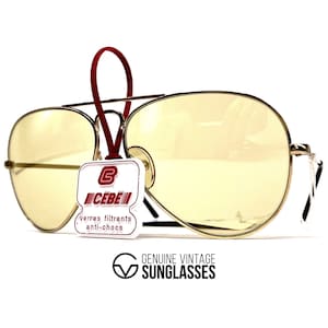 May include: Vintage gold-tone aviator sunglasses with yellow lenses. The sunglasses have a red tag attached with the brand name "CEBE" and the text "verres filtrants anti-chocs". The text "GENUINE VINTAGE SUNGLASSES" is also visible.