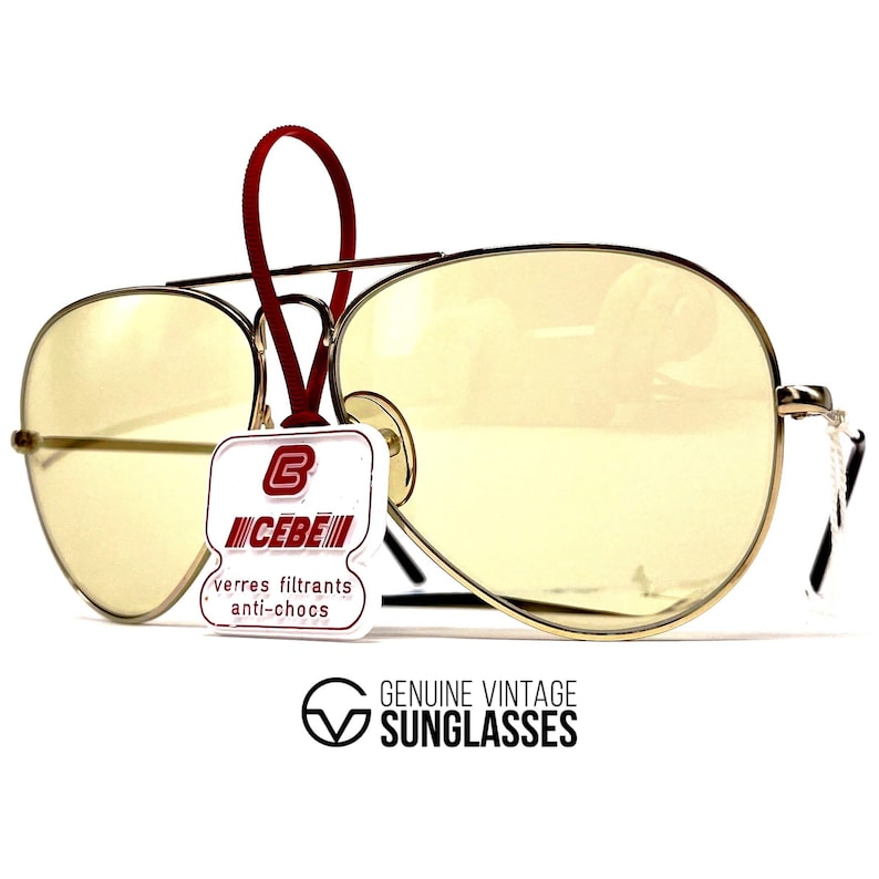 May include: Vintage gold-tone aviator sunglasses with yellow lenses. The sunglasses have a red tag attached with the brand name "CEBE" and the text "verres filtrants anti-chocs". The text "GENUINE VINTAGE SUNGLASSES" is also visible.