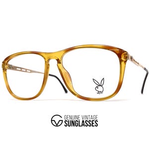 May include: Vintage eyeglasses with a light brown frame and clear lenses. The glasses feature a rectangular shape with a keyhole bridge and the Playboy bunny logo on the right lens. The temples are thin and metallic. The text "GENUINE VINTAGE SUNGLASSES" is at the bottom.