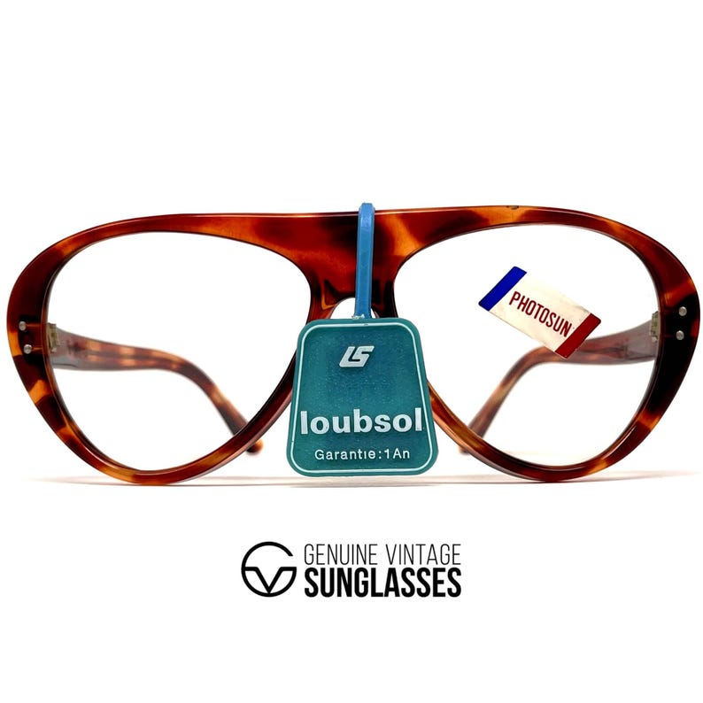 May include: Vintage tortoiseshell eyeglasses with a distinctive shape. The frames have a warm brown and amber pattern. A blue tag reads "loubsol Garantie:1An" and a small tag with "PHOTOSUN" is attached. The text "GENUINE VINTAGE SUNGLASSES" is below.