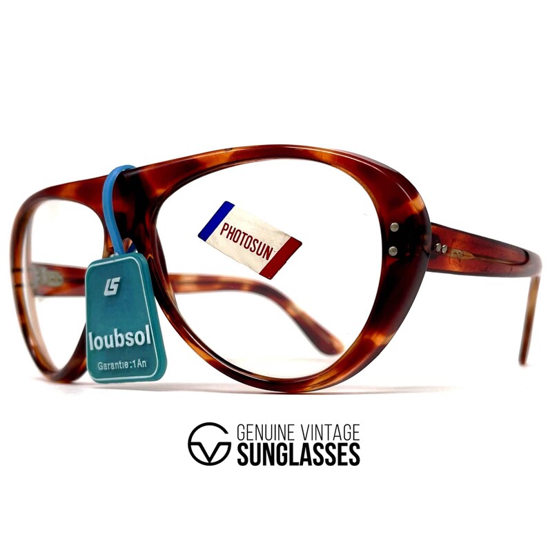 May include: Vintage tortoiseshell eyeglasses with a large, rounded frame. The glasses have a blue tag that reads "loubsol" and a small tag that reads "PHOTOSUN". The frame is brown with a marbled pattern. The text "GENUINE VINTAGE SUNGLASSES" is at the bottom.