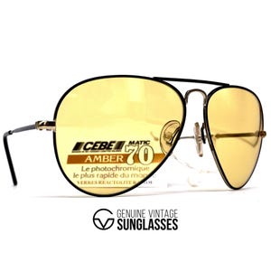 May include: Vintage CEBE MATIC Amber 70 sunglasses with yellow tinted lenses. The aviator-style frames have a black top bar and temples, with a silver-tone bridge and nose pads. The text on the lens reads "Le photochromique le plus rapide du mon".