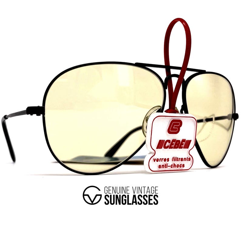 Puede incluir: Gafas de sol de aviador con montura negra y lentes de color amarillo. Las gafas de sol tienen una etiqueta roja con la marca "CEBE" y el texto "verres filtrants anti-chocs". La parte inferior de la imagen tiene el texto "GENUINE VINTAGE SUNGLASSES".