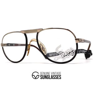 May include: Vintage Carrera Sport eyeglasses with a gold and black frame. The glasses have a double bridge design and clear lenses. The Carrera Sport logo is visible on the temple. The bottom of the image has the text "GENUINE VINTAGE SUNGLASSES".