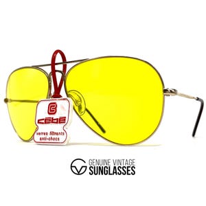 Puede incluir: Gafas de sol aviador vintage con lentes amarillas brillantes y montura plateada. Una etiqueta roja con la marca "CEBE" est&aacute; adjunta. El texto "GENUINE VINTAGE SUNGLASSES" est&aacute; impreso debajo.