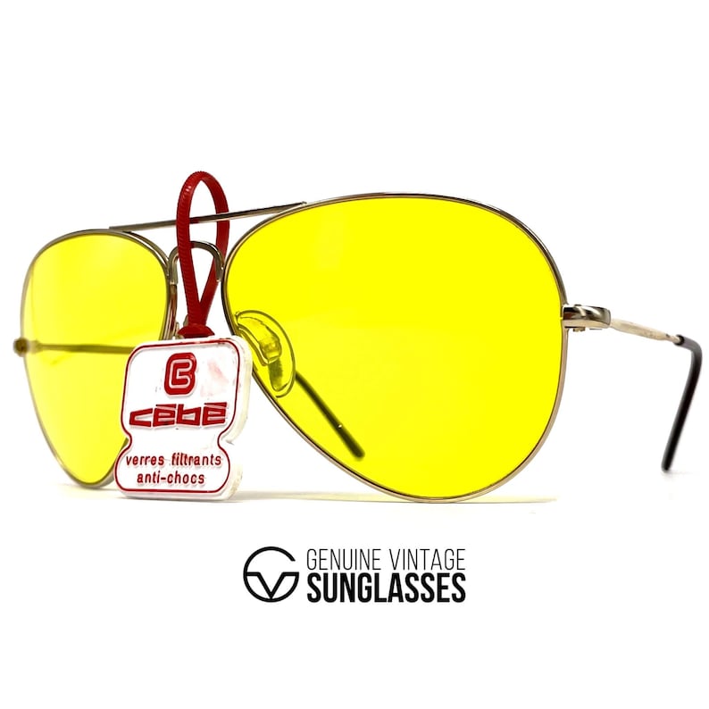 Puede incluir: Gafas de sol aviador vintage con lentes amarillas brillantes y montura plateada. Una etiqueta roja con la marca "CEBE" est&aacute; adjunta. El texto "GENUINE VINTAGE SUNGLASSES" est&aacute; impreso debajo.