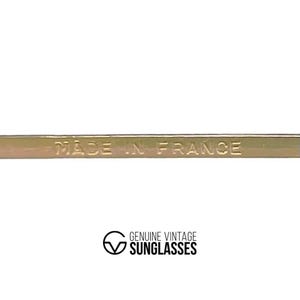 Puede incluir: Primer plano de una montura met&aacute;lica dorada con el texto en relieve "MADE IN FRANCE". Debajo, el logotipo dice "GENUINE VINTAGE SUNGLASSES" en una fuente serif. La montura es probablemente para gafas o gafas de sol.