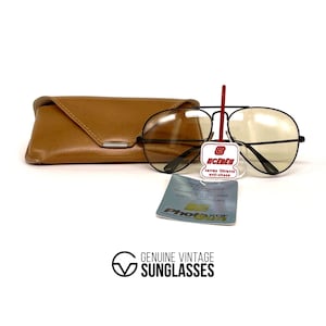 Puede incluir: Gafas de sol aviador negras vintage con lentes de color amarillo, un estuche de cuero marr&oacute;n y una etiqueta del producto. Las gafas de sol tienen un doble puente y un dise&ntilde;o cl&aacute;sico. La etiqueta dice "UCEBEN" y "verres filtrants anti-chocs".