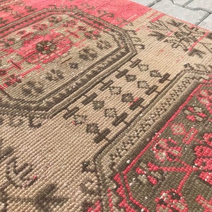 Puede incluir: Una alfombra vintage con un patr&oacute;n geom&eacute;trico en tonos marrones, rosas y blancos. La alfombra tiene un aspecto desgastado y est&aacute; hecha de un material suave y tejido.