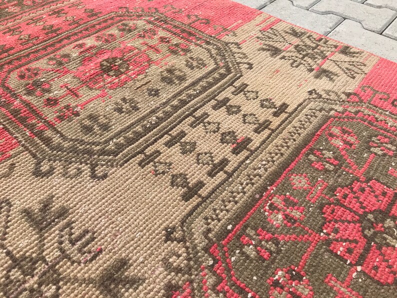 Puede incluir: Una alfombra vintage con un patr&oacute;n geom&eacute;trico en tonos marrones, rosas y blancos. La alfombra tiene un aspecto desgastado y est&aacute; hecha de un material suave y tejido.