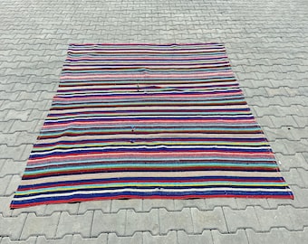 Pode incluir: Um tapete listrado colorido com uma variedade de cores, incluindo vermelho, azul, amarelo e verde. O tapete é feito de tecido tecido e tem um visual ligeiramente desgastado.