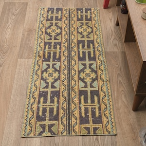 May include: A long, narrow rug with a geometric pattern in shades of brown, yellow, and blue. The rug has a traditional design with repeating motifs.