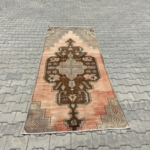 May include: A vintage rug with a geometric pattern in shades of brown, pink, and beige. The rug has a faded, distressed look and is laid out on a grey concrete surface.
