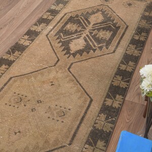 Puede incluir: Una alfombra de pasillo beige y marr&oacute;n con un patr&oacute;n geom&eacute;trico. La alfombra tiene un aspecto desgastado y est&aacute; hecha de un material suave y tejido.