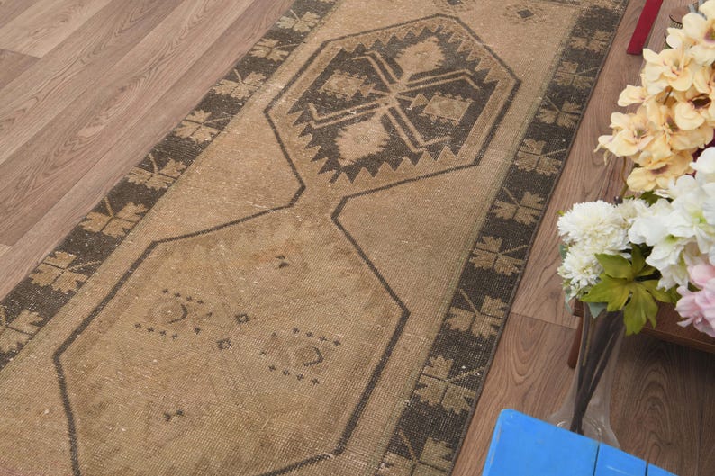 Puede incluir: Una alfombra de pasillo beige y marr&oacute;n con un patr&oacute;n geom&eacute;trico. La alfombra tiene un aspecto desgastado y est&aacute; hecha de un material suave y tejido.