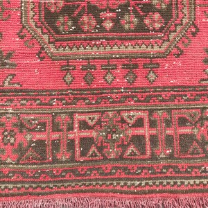 Puede incluir: Primer plano de una alfombra roja y marr&oacute;n con un patr&oacute;n y un borde con flecos. La alfombra tiene un aspecto descolorido y vintage.
