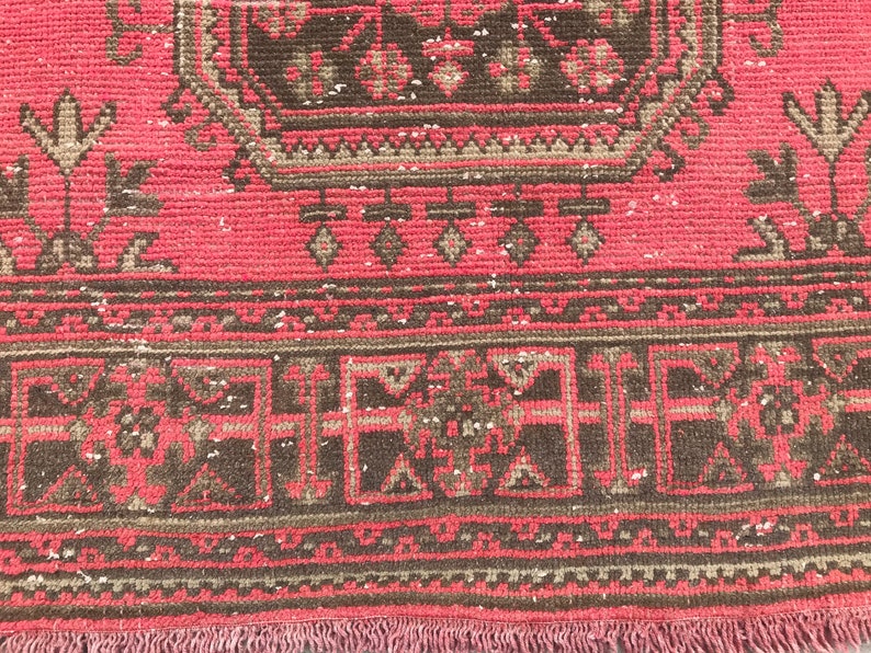 Puede incluir: Primer plano de una alfombra roja y marr&oacute;n con un patr&oacute;n y un borde con flecos. La alfombra tiene un aspecto descolorido y vintage.