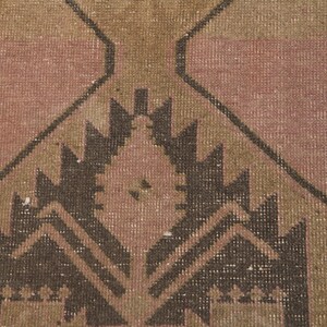 Puede incluir: Una alfombra vintage con un patr&oacute;n geom&eacute;trico en tonos marrones, rosas y beige. La alfombra tiene un aspecto desgastado y est&aacute; hecha de lana.