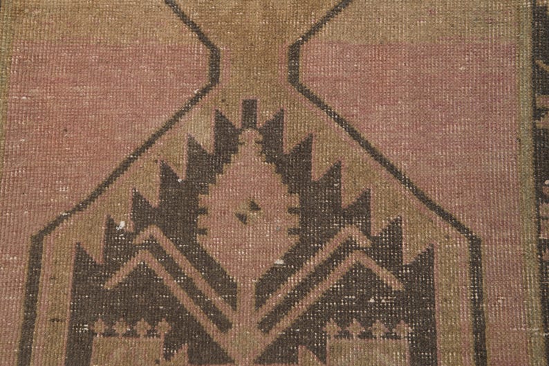Puede incluir: Una alfombra vintage con un patr&oacute;n geom&eacute;trico en tonos marrones, rosas y beige. La alfombra tiene un aspecto desgastado y est&aacute; hecha de lana.