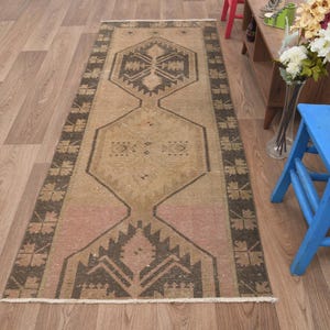 Puede incluir: Un tapete corredor beige y marr&oacute;n con un dise&ntilde;o geom&eacute;trico. La alfombra tiene un aspecto descolorido y vintage y est&aacute; hecha de lana.
