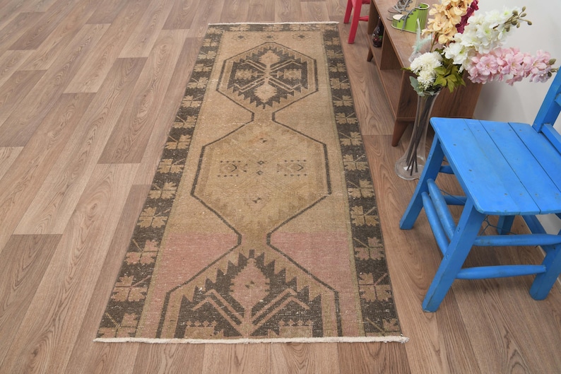 Puede incluir: Un tapete corredor beige y marr&oacute;n con un dise&ntilde;o geom&eacute;trico. La alfombra tiene un aspecto descolorido y vintage y est&aacute; hecha de lana.