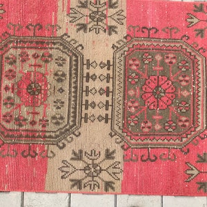 Puede incluir: Una alfombra turca vintage de color rosa y beige. La alfombra presenta un patr&oacute;n geom&eacute;trico con detalles intrincados. La alfombra est&aacute; en buen estado con algunas se&ntilde;ales de desgaste.