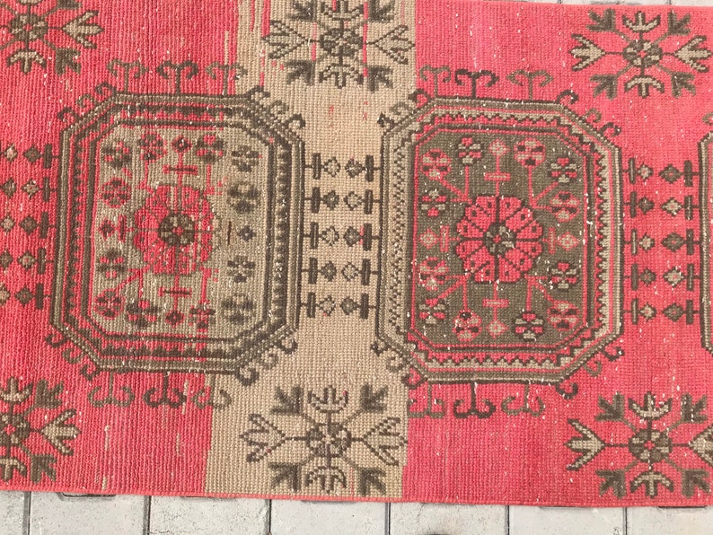 Puede incluir: Una alfombra turca vintage de color rosa y beige. La alfombra presenta un patr&oacute;n geom&eacute;trico con detalles intrincados. La alfombra est&aacute; en buen estado con algunas se&ntilde;ales de desgaste.