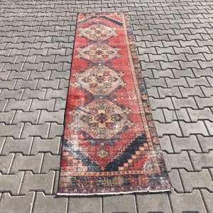 May include: A long, narrow red and blue rug with a traditional Persian design. The rug has a faded, vintage look and is made of wool.