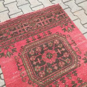 Puede incluir: Una alfombra vintage roja y marr&oacute;n con un patr&oacute;n geom&eacute;trico. La alfombra tiene un aspecto descolorido y est&aacute; hecha de lana.