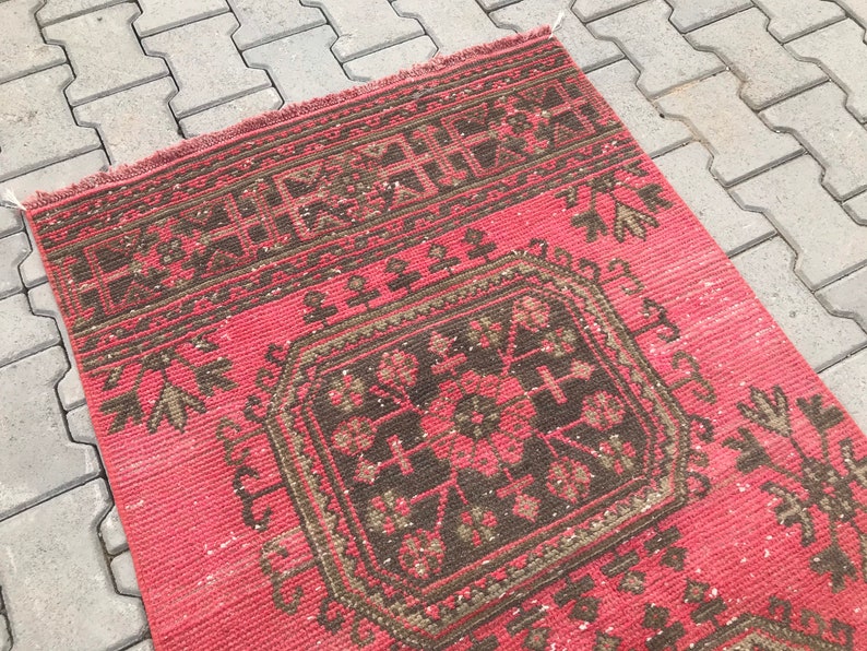 Puede incluir: Una alfombra vintage roja y marr&oacute;n con un patr&oacute;n geom&eacute;trico. La alfombra tiene un aspecto descolorido y est&aacute; hecha de lana.