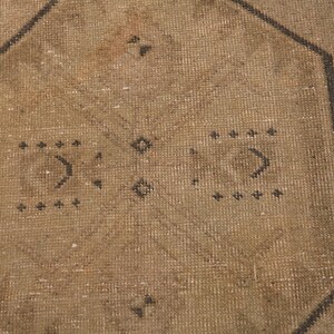 Puede incluir: Primer plano de una alfombra marr&oacute;n con un patr&oacute;n geom&eacute;trico en negro. La alfombra tiene un aspecto desgastado y vintage.
