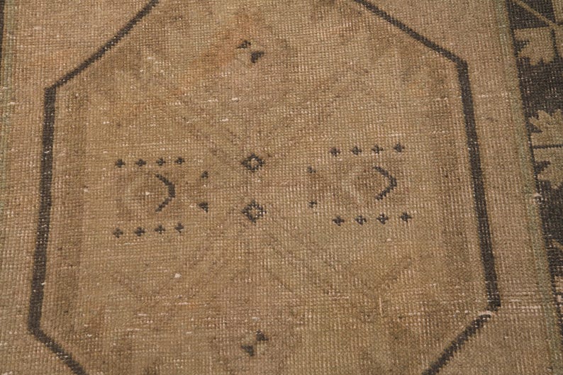Puede incluir: Primer plano de una alfombra marr&oacute;n con un patr&oacute;n geom&eacute;trico en negro. La alfombra tiene un aspecto desgastado y vintage.