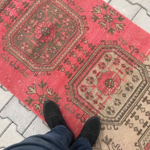 Puede incluir: Una alfombra de color rosa y beige con dise&ntilde;os intrincados. La alfombra tiene un aspecto desgastado y est&aacute; hecha de fibras tejidas.