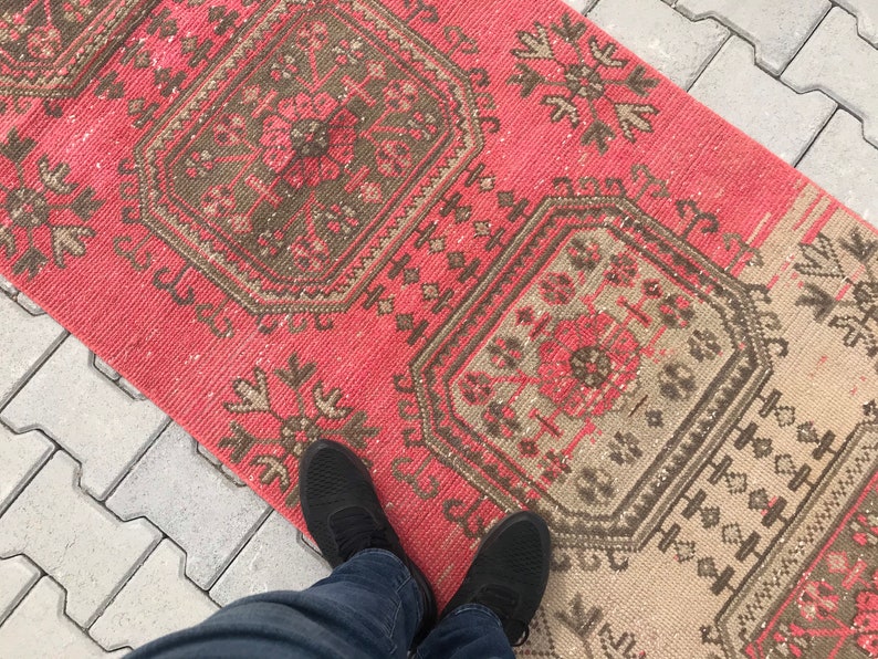 Puede incluir: Una alfombra de color rosa y beige con dise&ntilde;os intrincados. La alfombra tiene un aspecto desgastado y est&aacute; hecha de fibras tejidas.