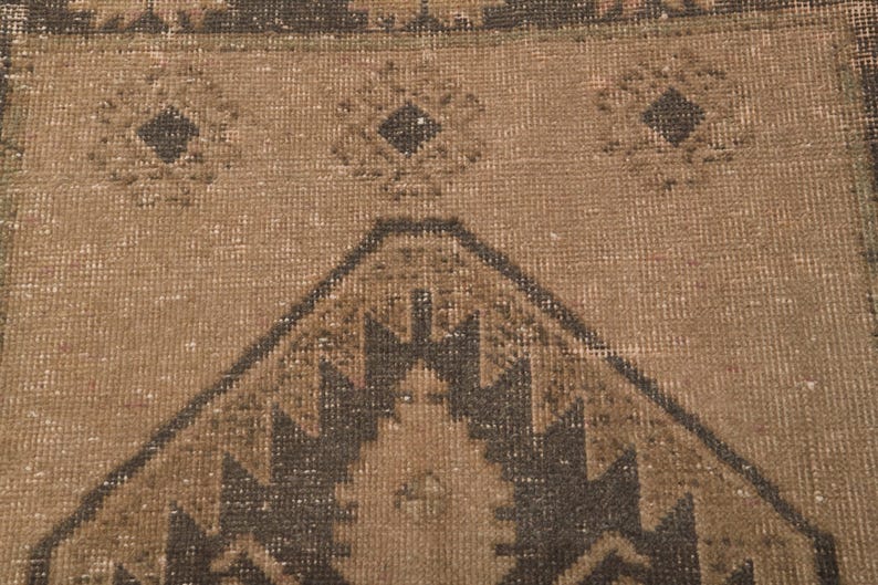 Puede incluir: Primer plano de una alfombra marr&oacute;n y negra con un dise&ntilde;o geom&eacute;trico. La alfombra tiene un aspecto desgastado y vintage.