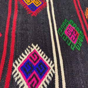 Pode incluir: Um tapete preto e branco com um padr&atilde;o geom&eacute;trico em tons de rosa, azul, verde, laranja e amarelo. O tapete tem um design tradicional com motivos repetidos.
