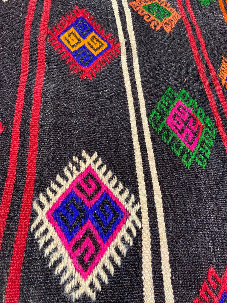 Pode incluir: Um tapete preto e branco com um padr&atilde;o geom&eacute;trico em tons de rosa, azul, verde, laranja e amarelo. O tapete tem um design tradicional com motivos repetidos.
