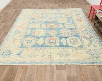 Könnte beinhalten: Ein großer, rechteckiger Teppich mit einem blauen Mittelfeld und einem cremefarbenen Rand. Der Teppich zeigt aufwendige Blumen- und geometrische Muster in Blau-, Pfirsich- und Grautönen. Er liegt auf einem Holzboden.