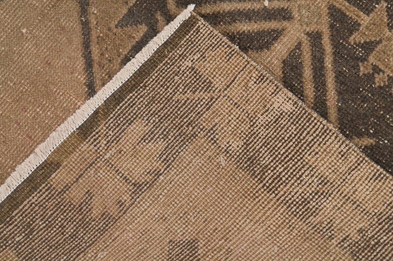 Puede incluir: Primer plano de una alfombra marr&oacute;n y beige con un patr&oacute;n geom&eacute;trico. La alfombra tiene un borde de flecos.