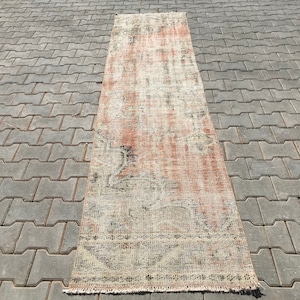May include: A long, rectangular rug with a faded, distressed look. The rug has a light pink background with a white and grey pattern. The rug has a fringe border.