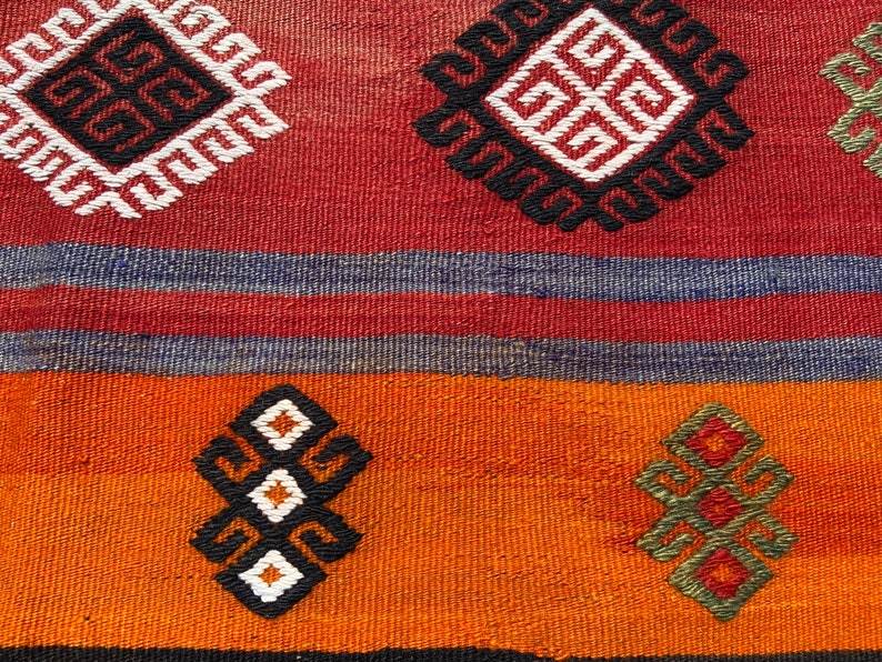 Pode incluir: Um close-up de um tapete tecido colorido com padr&otilde;es geom&eacute;tricos em tons de vermelho, laranja, azul, preto e branco.