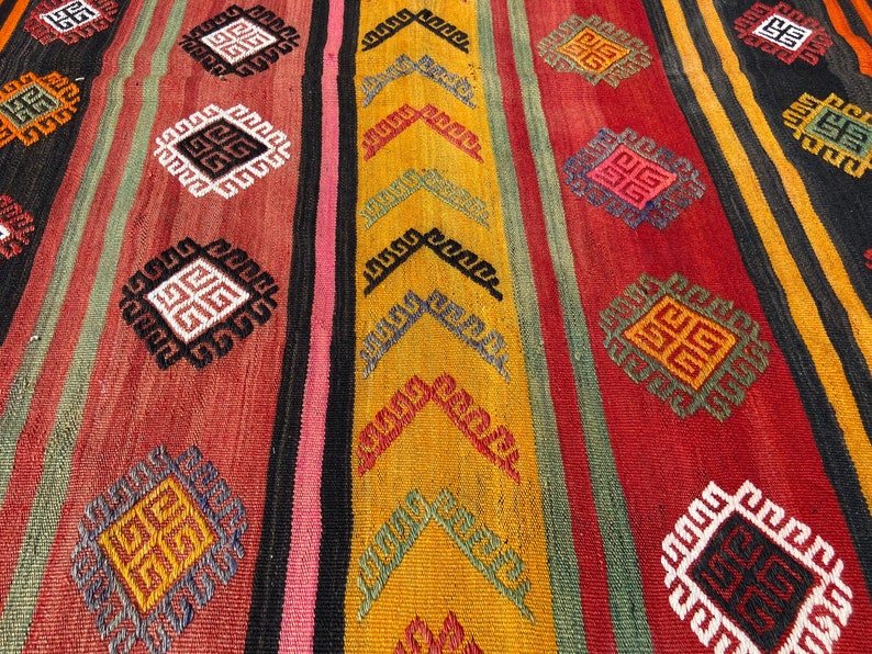 Pode incluir: Um tapete tecido colorido com um padr&atilde;o geom&eacute;trico em tons de vermelho, verde, amarelo e preto.