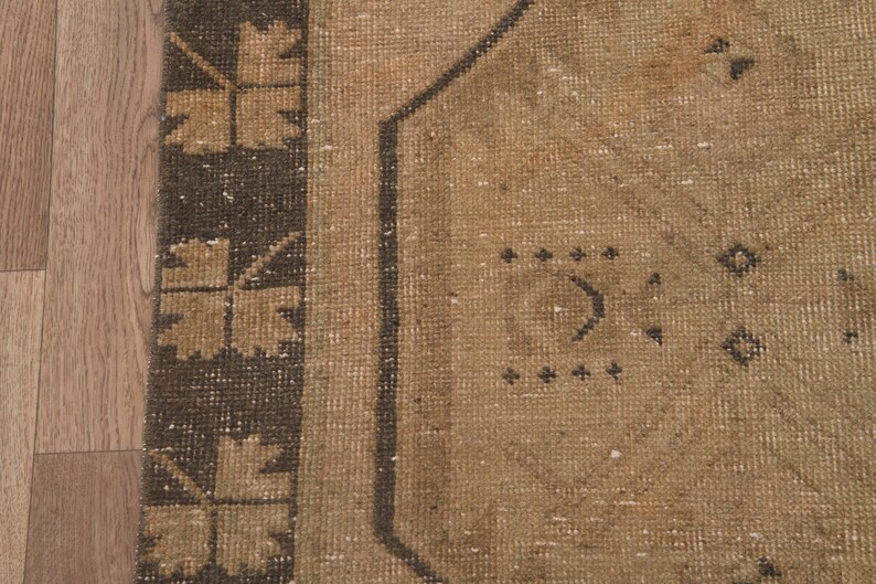 Puede incluir: Primer plano de una alfombra beige con un patr&oacute;n geom&eacute;trico marr&oacute;n. La alfombra tiene un aspecto desgastado y vintage.