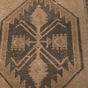 Puede incluir: Una alfombra vintage con un patr&oacute;n geom&eacute;trico marr&oacute;n y beige. La alfombra tiene un aspecto desgastado y envejecido, lo que le da un aspecto r&uacute;stico y antiguo.