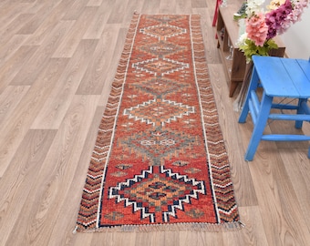 Könnte beinhalten: Ein roter, orangefarbener und blauer Läufer mit einem Fransenrand. Der Läufer hat ein traditionelles Design mit geometrischen Formen und einem zentralen Medaillon.