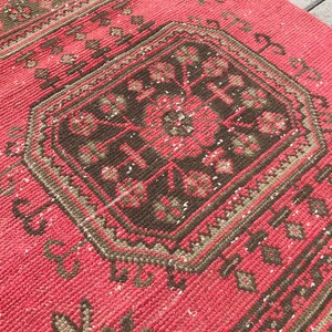 Puede incluir: Una alfombra roja y marr&oacute;n con un dise&ntilde;o geom&eacute;trico. La alfombra tiene un aspecto desgastado y est&aacute; hecha de un material tejido.